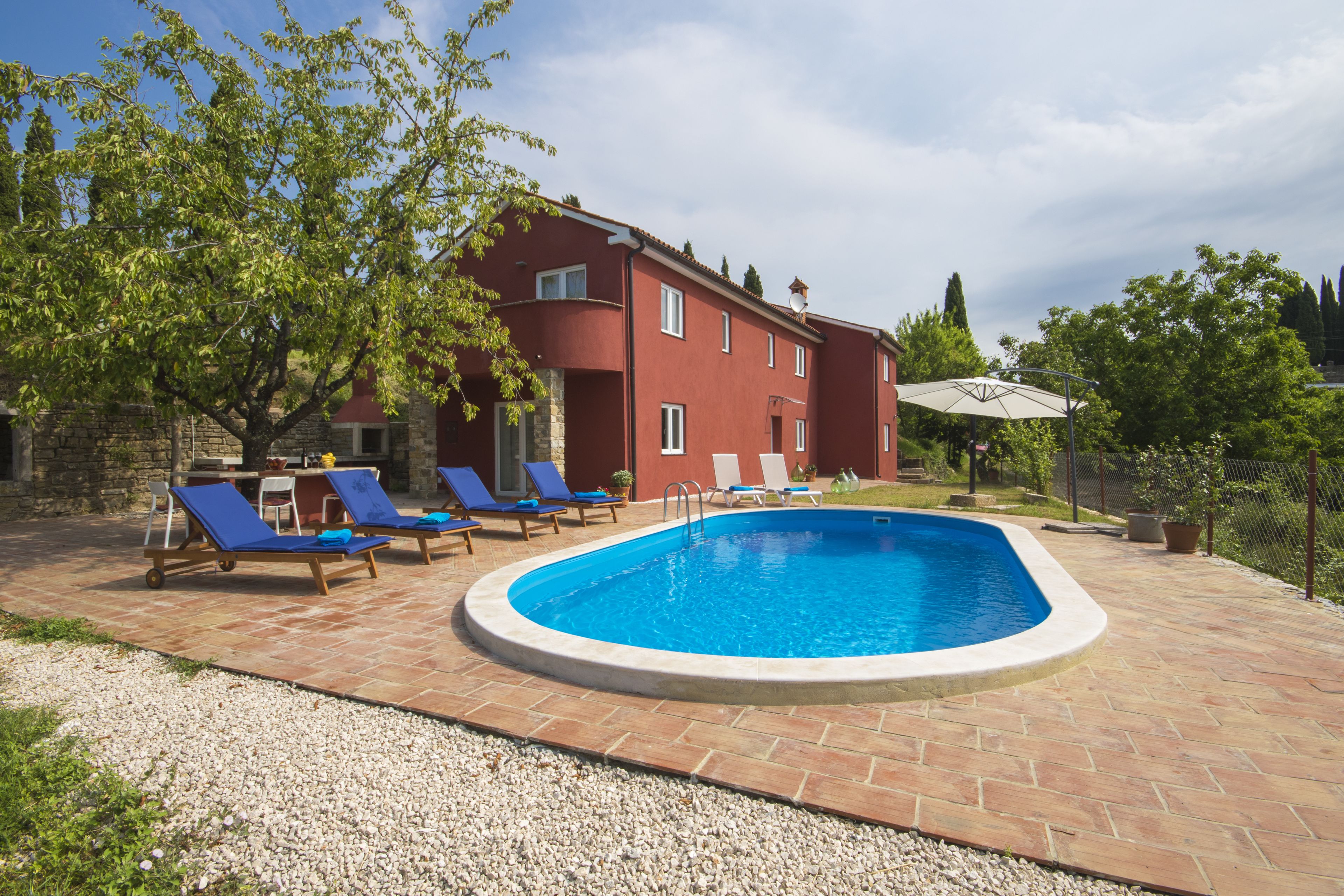 A swimming pool with lounge chairs, a stone patio, and a red building in the background.