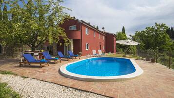 A swimming pool with lounge chairs, a stone patio, and a red building in the background.