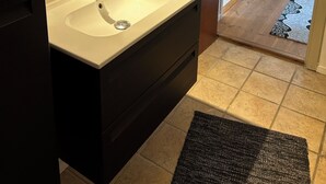 A bathroom with a white sink, dark vanity, and a wooden door leading to a hallway with a patterned rug. - Nice holiday home near the beach (Rødekro)