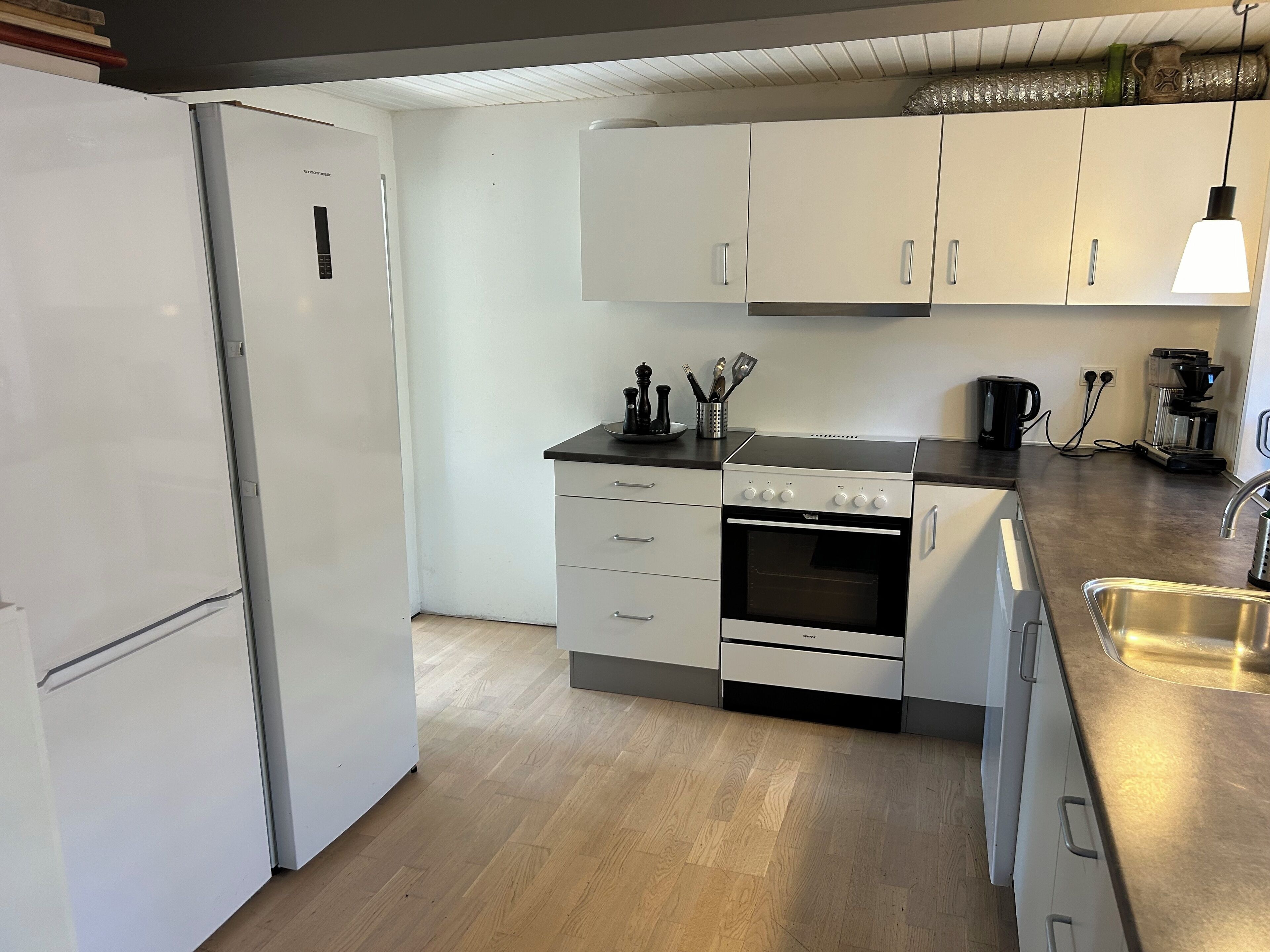 Een kleine keuken met witte kastjes, een inbouwoven en een roestvrijstalen spoelbak.