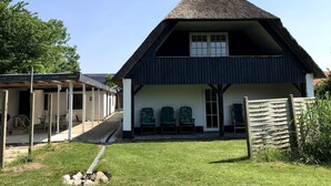A house with a thatched roof, a covered porch with chairs, and a grassy yard. - Nice holiday home near the beach (Rødekro)
