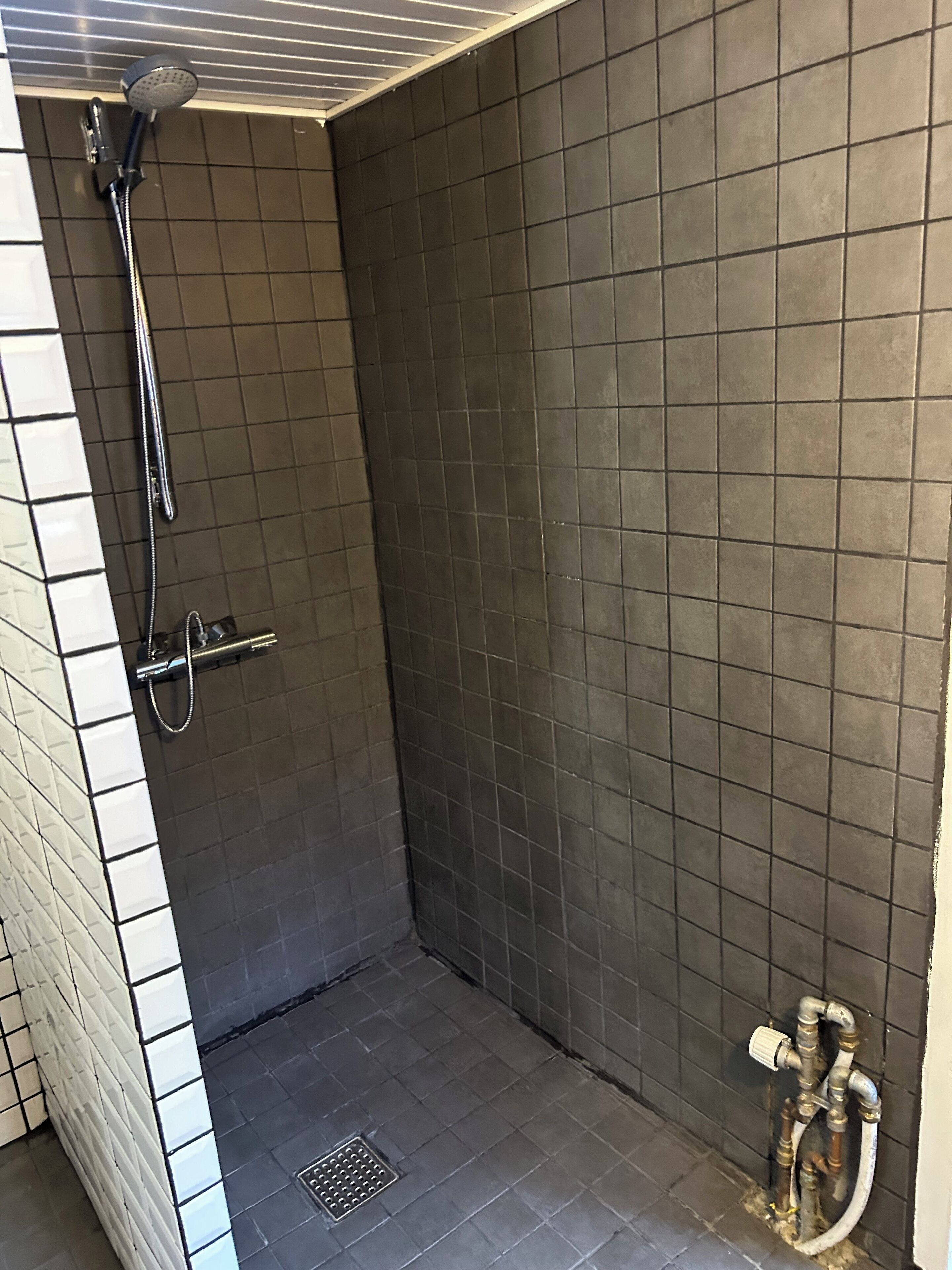 Un petit espace de douche carrelé, équipé d’un pommeau de douche à main et d’un robinet fixé au mur.