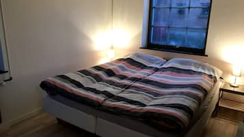 Een eenpersoonskamer met een gestreept beddegoed, twee bedlampen, een raam met uitzicht op gebouwen en een houten vloer.
