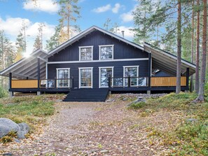 Een chalet met twee verdiepingen, een steile nok, grote ramen en een overdekt terras.