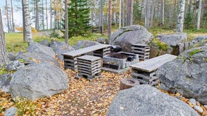Een camping met houten banken en een barbecueplaats, omringd door grote rotsen en bomen.