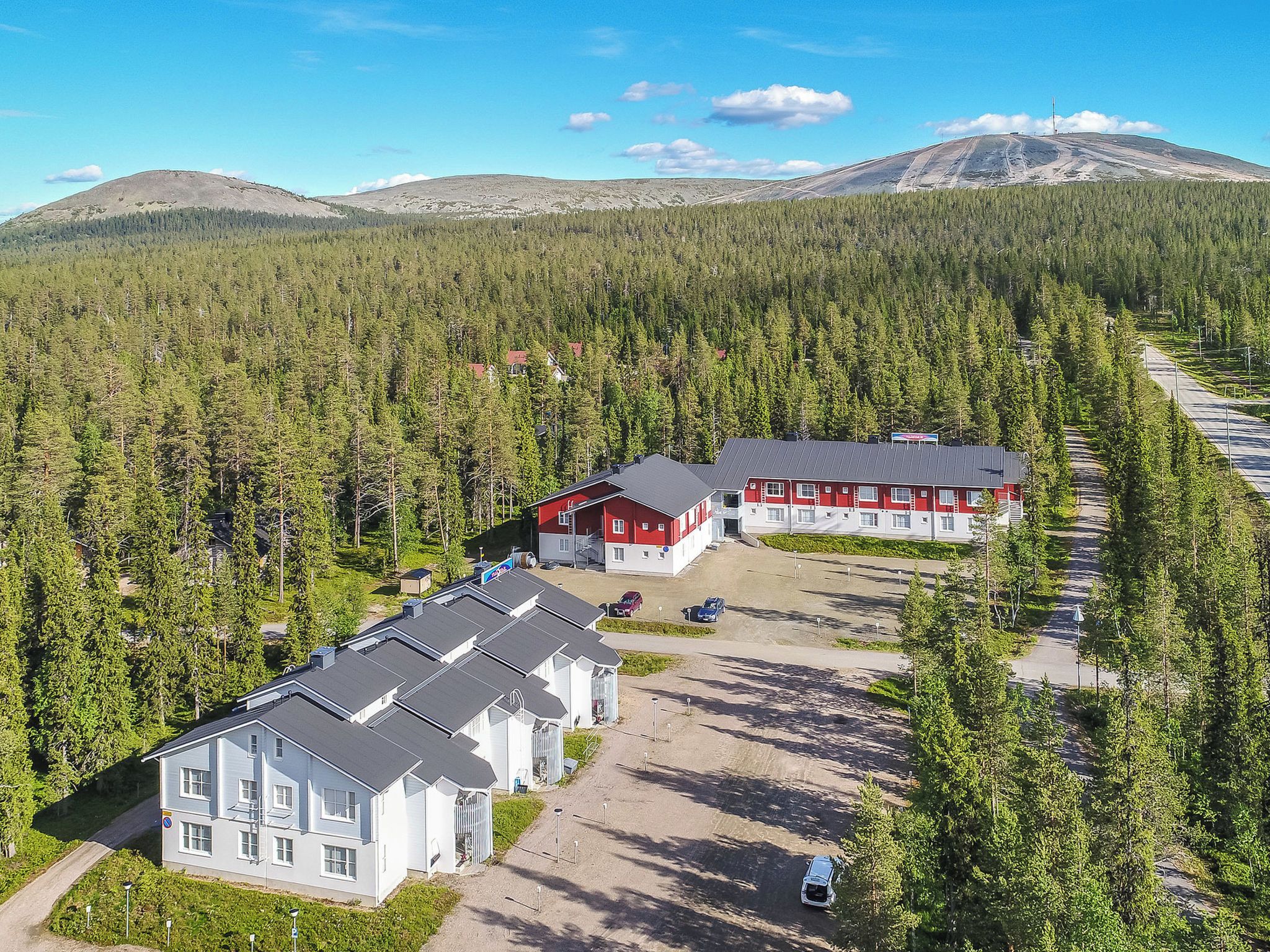 Un chalet comprenant plusieurs bâtiments, entouré d’une forêt dense et avec des montagnes en arrière-plan.