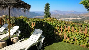 A terrace with white lounge chairs, a thatched umbrella, and a view of distant mountains and a valley. - El Cerrillo - Cerro Negro by Interhome (Orgiva)
