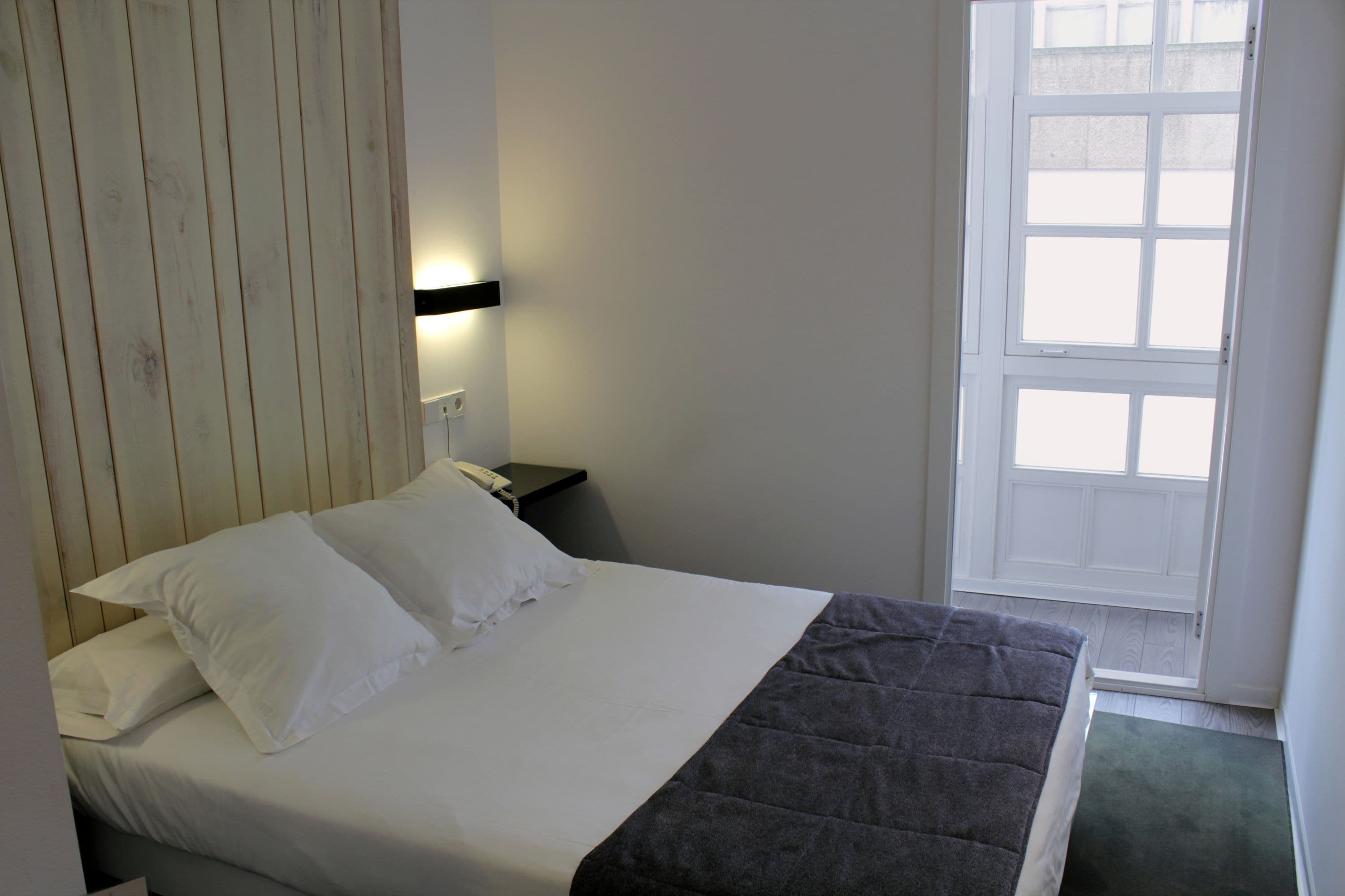 Une chambre d’hôtel avec un lit, une table de chevet, une lampe fixée au mur et une fenêtre.
