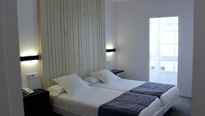 A double bed with a headboard, bedside tables, and a window with a view. - Hotel Lois (A Coruña)