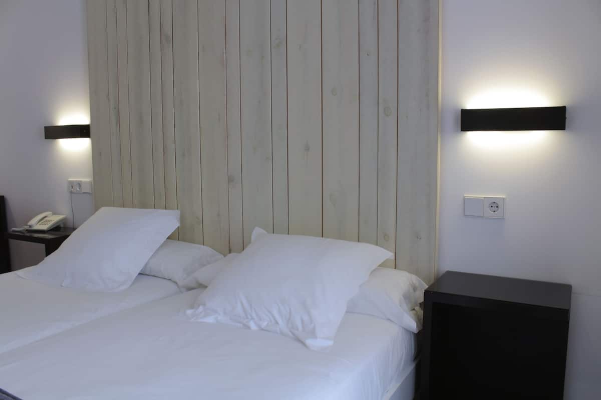 A hotel room with two beds, a wooden headboard, bedside tables with lamps, and a phone on one of the tables.