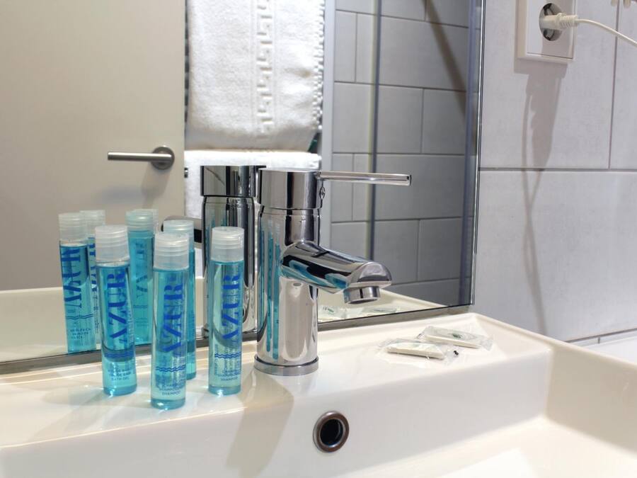 A bathroom with a white sink, a mirror, and several bottles of blue shampoo.