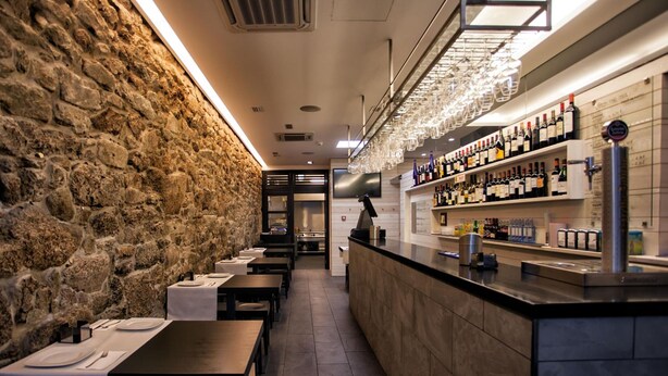A restaurant with stone walls, a bar area with shelves of bottles, and tables set for dining. - Hotel Lois (A Coruña)