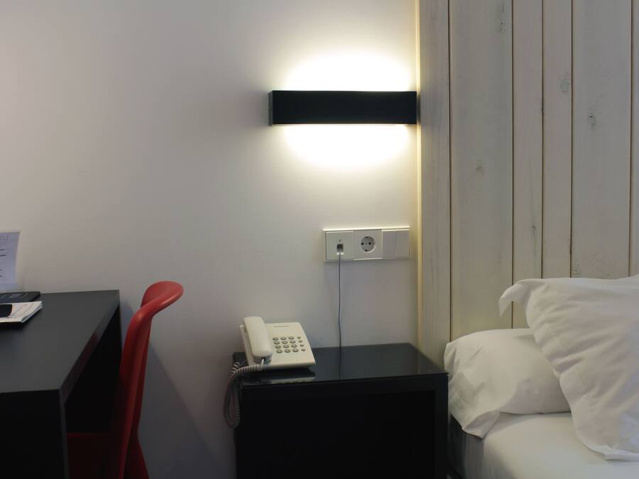 Una habitación de hotel con cama, un escritorio con teléfono, y una lámpara de pared.