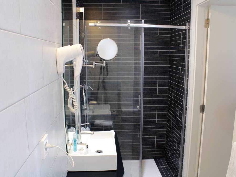 A modern bathroom with a glass shower enclosure, a white sink, and a hairdryer on the wall.