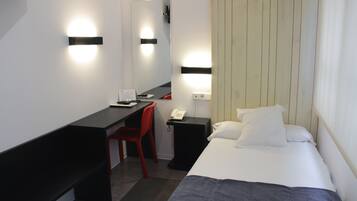 Une chambre d’hôtel comprenant un lit, un bureau, une chaise, une table de chevet avec un téléphone et des lampes fixées au mur.