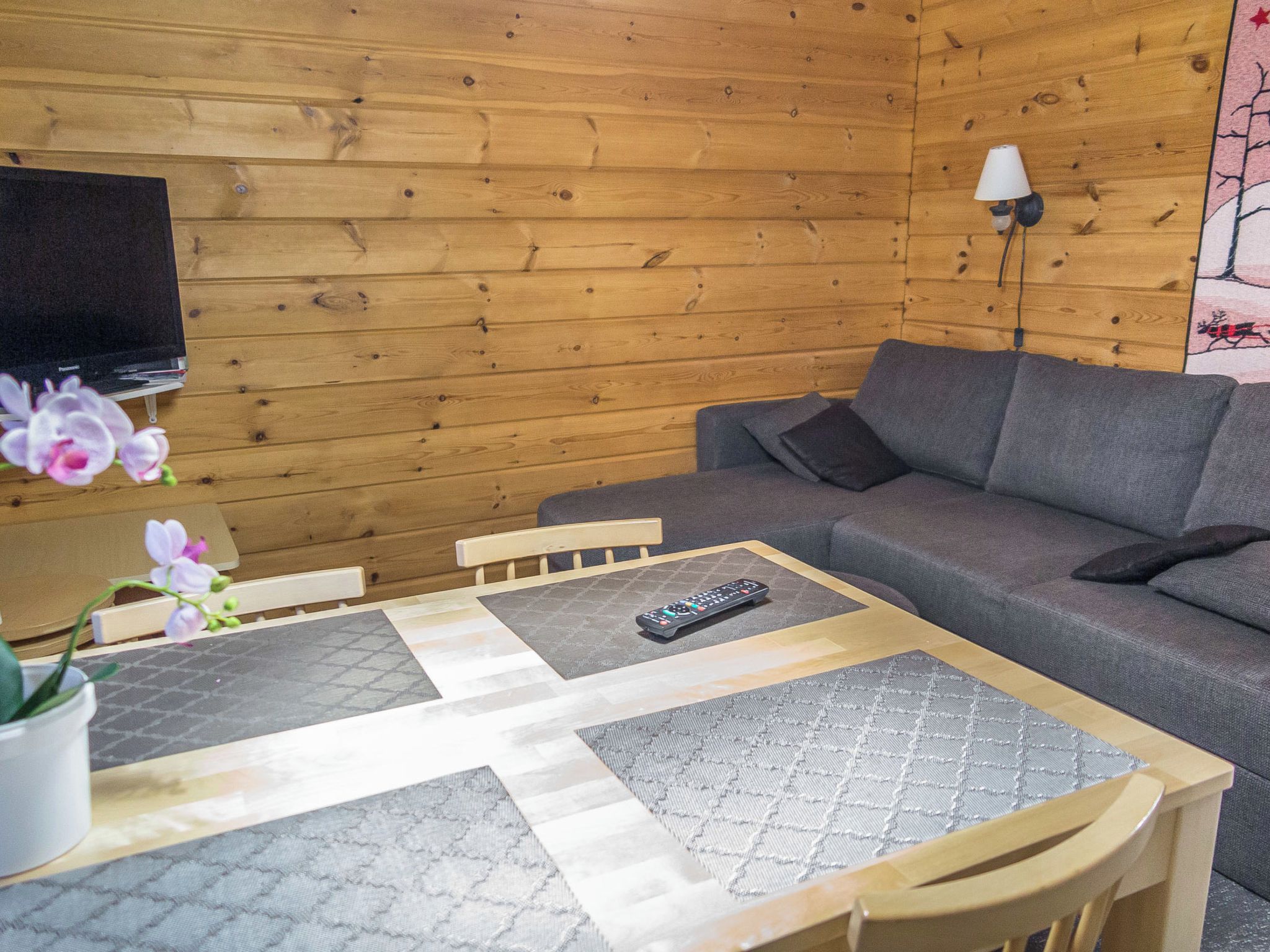 Et træpanelt interiør med en sofa, et fjernsyn ophængt på væggen og en fjernbetjening på et bord.