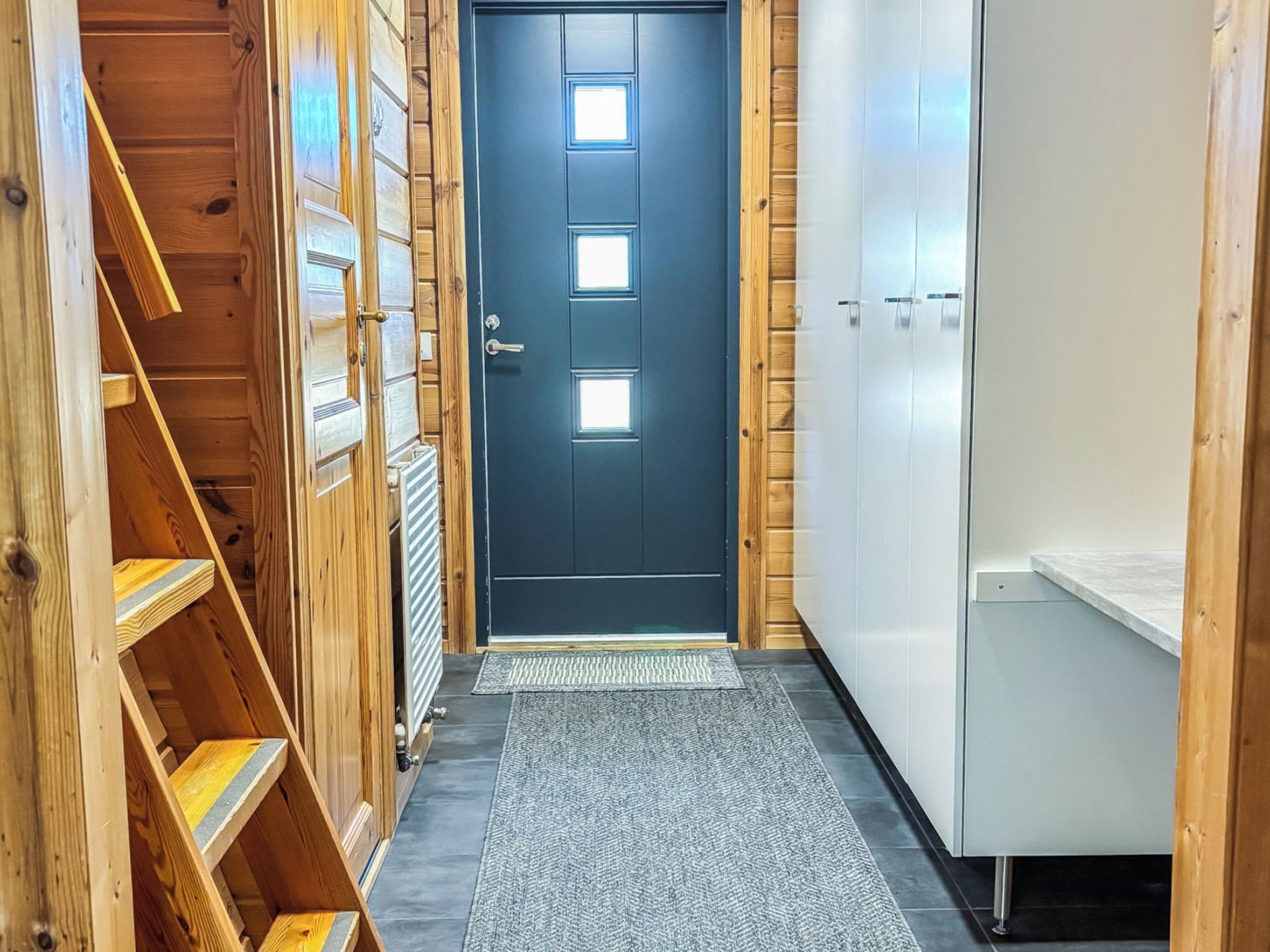 A narrow hallway with a dark blue door, wooden shelving, and a white cabinet.