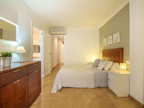 Un dormitorio con cama, mesitas de noche, cómoda, espejo y una planta en maceta.