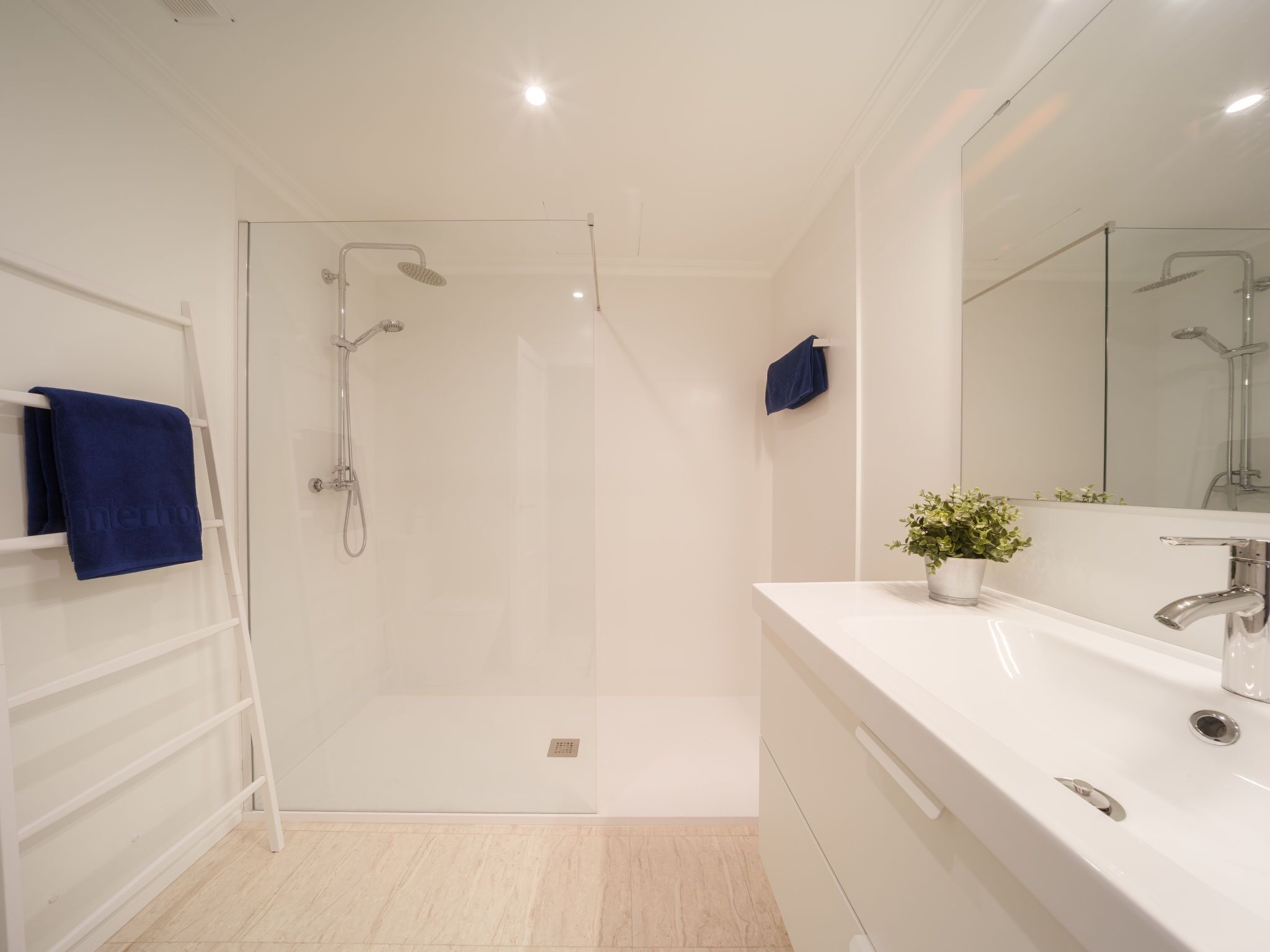 A modern bathroom with a glass-enclosed shower, a white vanity with a mirror, and a blue towel on a rack.