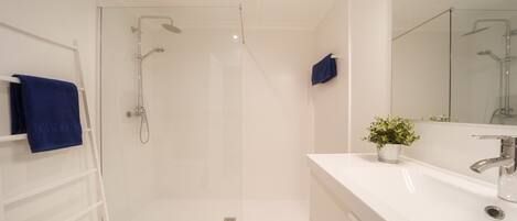 A modern bathroom with a glass-enclosed shower, a white vanity with a mirror, and a blue towel on a rack.