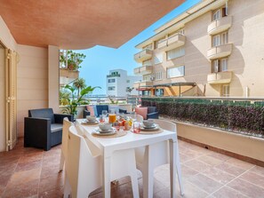 Un balcón con una mesa de comedor para dos personas, asientos exteriores y vistas a un edificio con balcones.