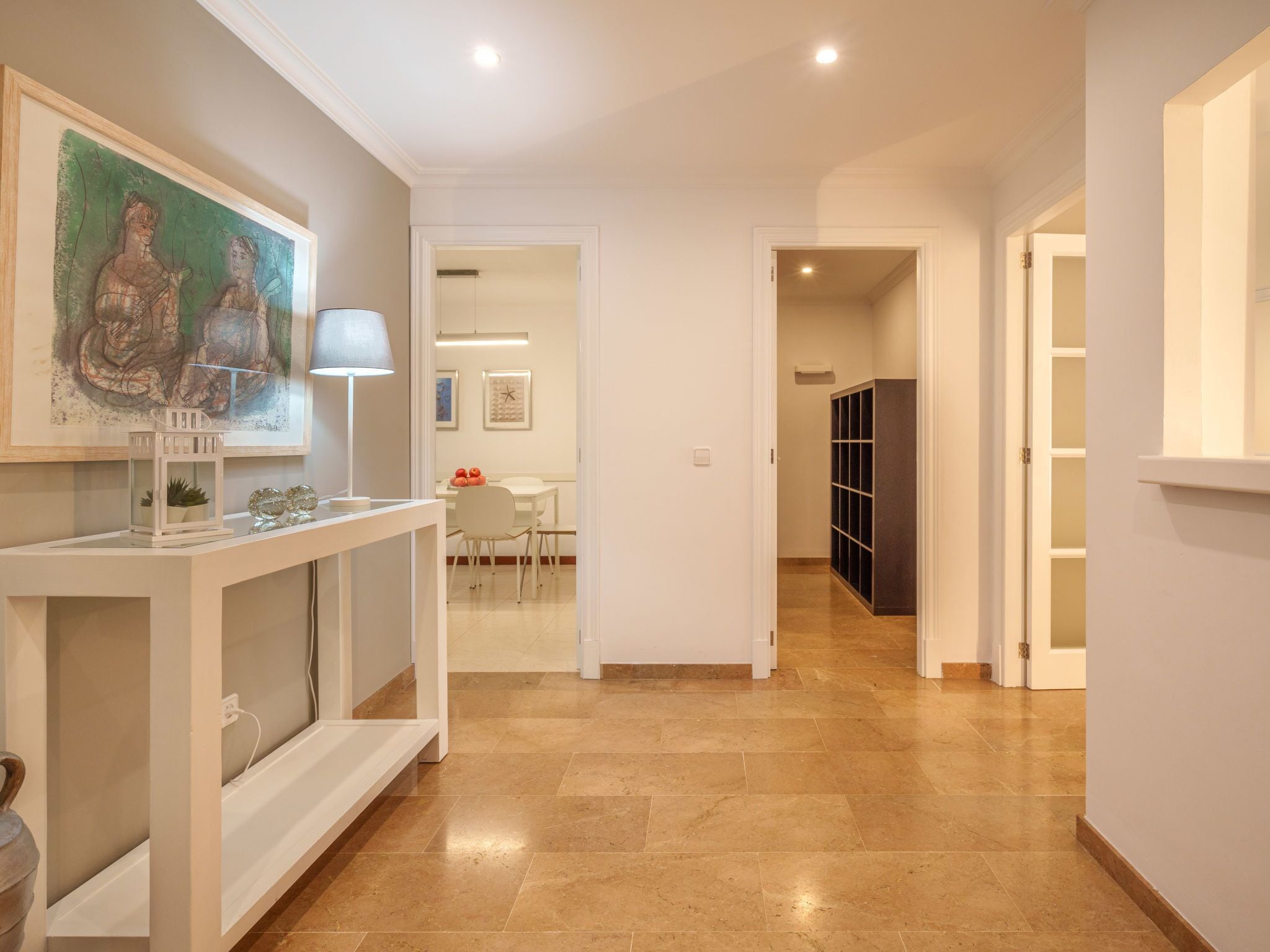 A hallway with a white console table, a painting, and a dark storage unit.
