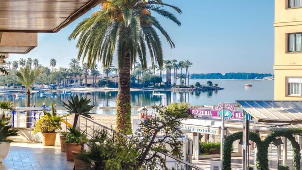 A waterfront view with a pool, palm trees, and a pizzeria sign. - Maritimo by Interhome (Port d'Alcúdia)