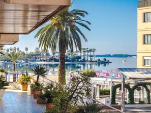 A waterfront view with a pool, palm trees, and a pizzeria sign. - Maritimo by Interhome (Port d'Alcúdia)