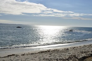 Une plage avec une eau calme, un ciel dégagé et une terre lointaine à l’horizon.