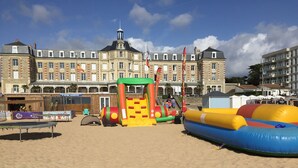 Ein Strand mit aufblasbaren Spielgeräten und einem historischen Gebäude im Hintergrund.