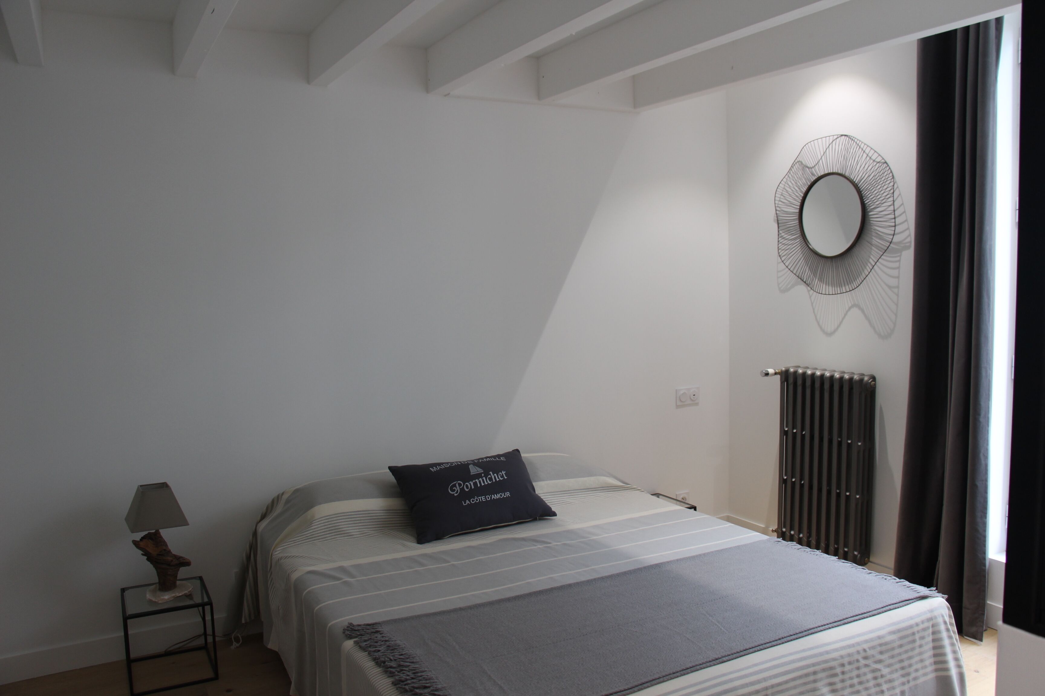 Ein Schlafzimmer mit einem Bett, einem Nachttisch mit Lampe, einem Wandspiegel und einer Heizung.