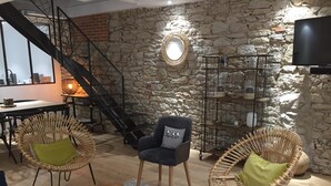 Ein gemütliches Wohnzimmer mit einer Steinwand, Korbsesseln, einer Couch, einem kleinen Tisch und einer Treppe.