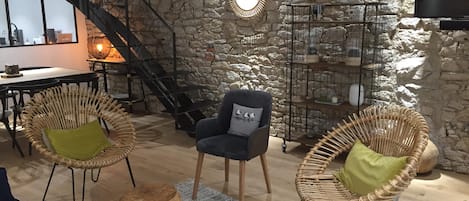 A cozy living room with a stone wall, wicker chairs, a sofa, a small table, and a staircase.
