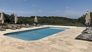 A rectangular swimming pool with lounge chairs and umbrellas, surrounded by a tiled deck.