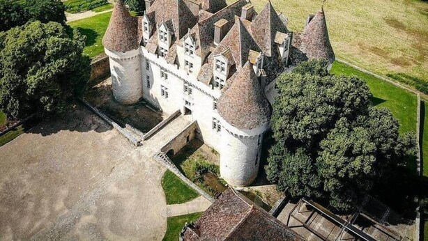 A castle with multiple towers, surrounded by well-maintained gardens and fields.