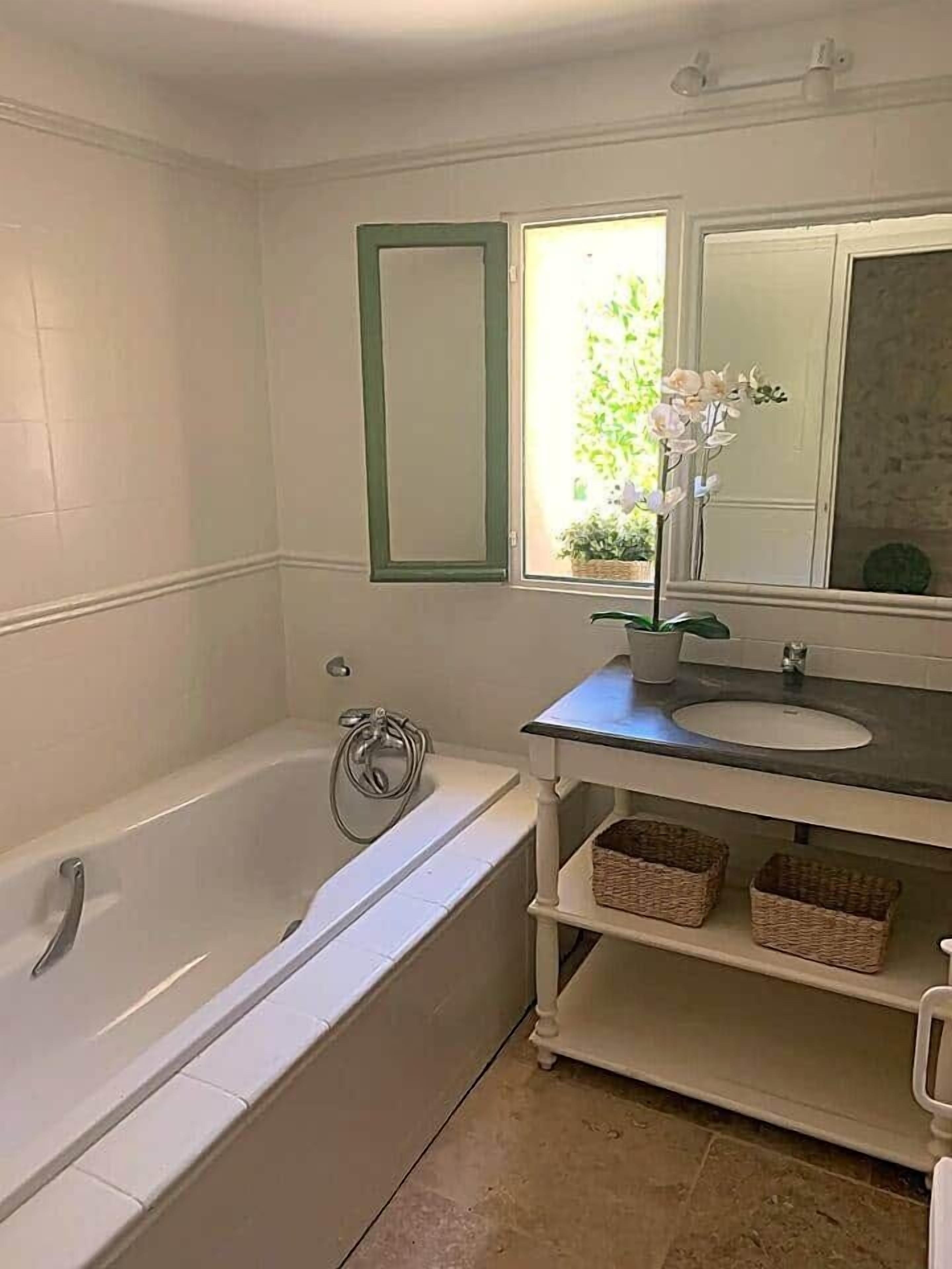 Ein Badezimmer mit einer Badewanne, einem Waschbecken, einem Spiegel und einem Fenster mit Blick auf Grünflächen.