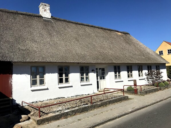 A white building with a thatched roof, multiple windows, and a small porch with a red railing.