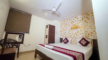 A hotel room with a bed, a ceiling fan, a window with blinds, a wall decoration, and a nightstand.