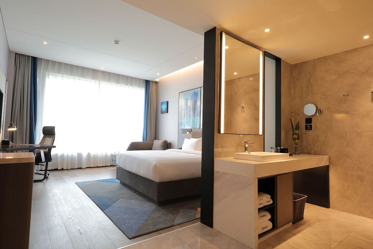 Una habitación de hotel moderna con una cama grande, un escritorio y un baño con tocador y espejo.