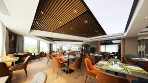 En moderne restaurant med høje lofter, trælameller og en blanding af orange og grå polstrede stole.