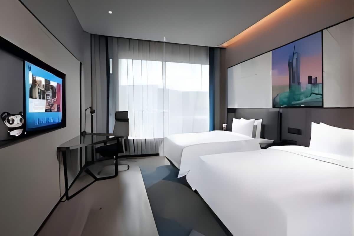 Una habitación de hotel moderna con dos camas, un escritorio, una silla y un televisor en la pared.