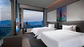 Et moderne hotelværelse med to senge, et stort vindue med byudsigt og et fladskærms-tv.