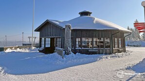 Una cabaña de madera con techo nevado y ventanas grandes, rodeada de nieve.