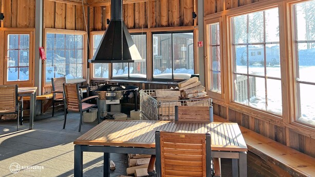 Un interior de madera con ventanas amplias, una mesa central y sillas.