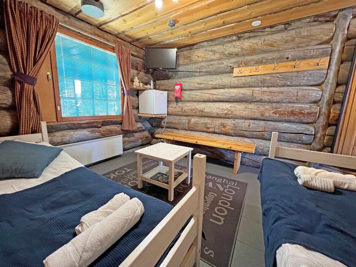 A cozy cabin-style room with two beds, a small table, a TV, and a window with curtains.