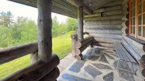 Una cabaña de troncos con un porche de baldosas de piedra y una valla de madera.