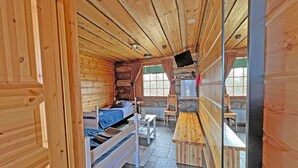 Interior de una cabaña de madera con una cama, una mesita y un banco.