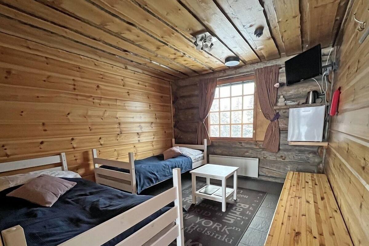 A cabin-style room with two wooden beds, a small table, a TV, and a window with curtains.