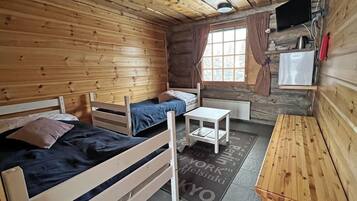 Mökkihenkinen huone, jossa on kaksi puista sänkyä, pieni pöytä, televisio ja ikkuna, jossa on verhot.