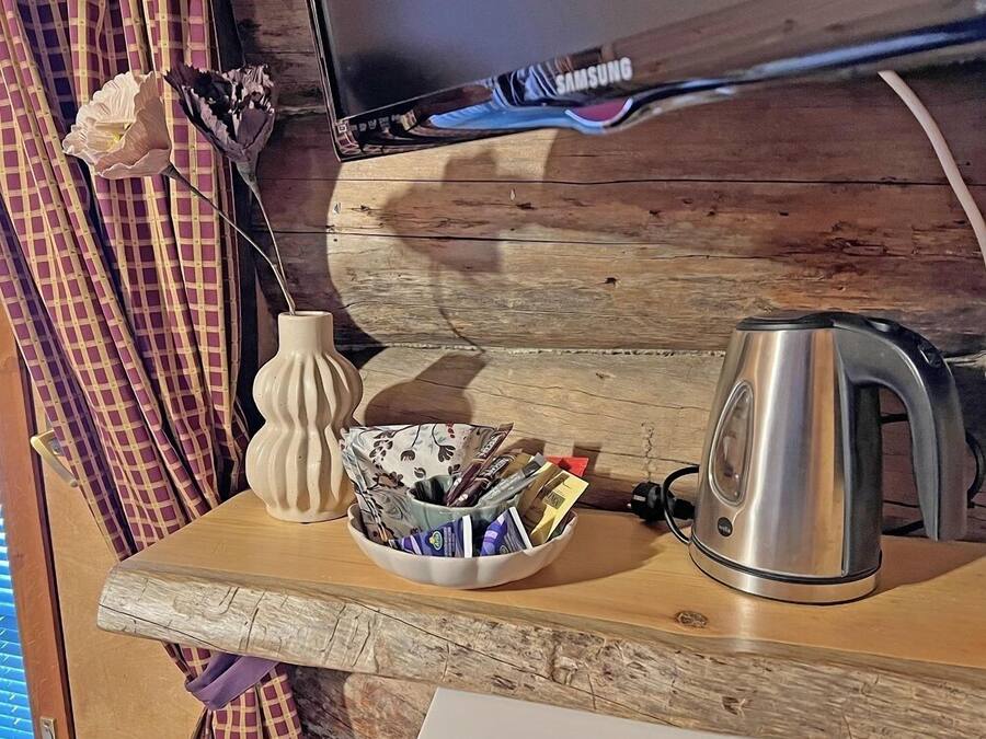 Una mesa de madera con un bol de bolígrafos, un jarrón blanco, una tetera y un televisor que muestra el logotipo de Samsung.